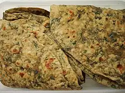 A stack of parathas that have a large amount of herbs mixed baked into the dough