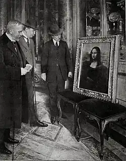 Three men in suits and hats stand examining the framed Mona Lisa painting displayed on two benches in an ornate room
