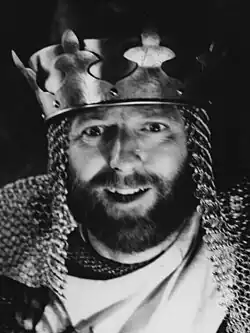 A black-and-white bust-length photo of Chapman as King Arthur