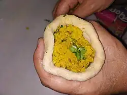 A thick circle of dough is folded around a filling of dal and herbs.