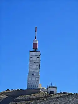 White and red summit communications tower on the rocky peak of Mont Ventoux under a clear blue sky