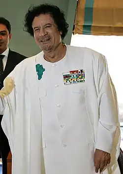 A middle-aged man, with black hair and facial stubble, wearing a white robe