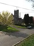 Stone building with square tower. In the foreground is a road.
