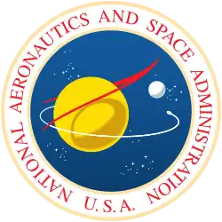 A blue sphere with stars, a yellow planet with a white moon; a red chevron representing wings, and an orbiting spacecraft; surrounded by a white border with "NATIONAL AERONAUTICS AND SPACE ADMINISTRATION U.S.A." in red letters.
