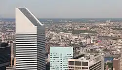 The slanted top of 601 Lexington Avenue, in the left foreground, as seen from Rockefeller Center. Other nearby skyscrapers are visible in the right foreground, while the borough of Queens is visible in the distance.