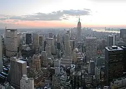 Aerial photo of skyscrapers and other buildings with a sunset or sunrise and partly cloudy sky in the background.