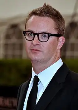 A photograph of filmmaker Nicholas Winding Refn, wearing glasses and a suit with bow tie.