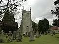 Stone church tower with flag pole. In the foreground are gravestones on grass.