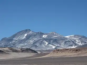 Photo: A broad, irregular mountain in an unvegetated landscape with sparse snow patches