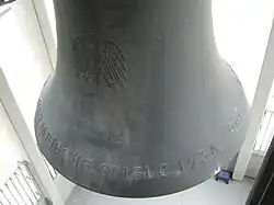 A large bell inscribed with text and the Olympic rings