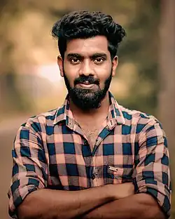 A Malayali man with a beard, wearing a checkered shirt, with his arms crossed in 2018