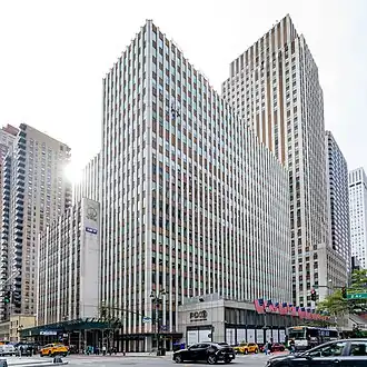 The Daily News Building's facade as viewed from Second Avenue and 42nd Street, looking southwest. The building is a rectangular tower with a white-brick facade, interspersed with vertical bands of windows and dark-colored spandrel panels. There are several setbacks on the facade.