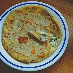 A round paratha with a piece broken off to show a filling of paneer and herbs