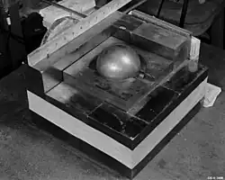 A square base of metal blocks, with a smaller square of metal on the top in the center, a Cooper block (the "core") contained in its center. A ruler along one side of the base shows roughly 10.5 inches (270&nbsp;mm) square.
