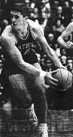 A man in a Kentucky Wildcats men's basketball jersey holding a ball during a game.