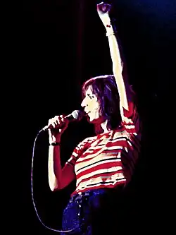 A color photograph of Patti Smith on stage with a microphone