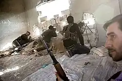 Four Kurdish soldiers in active combat, shooting through a makeshift hole in a building