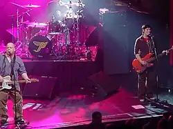 Kim Deal playing bass at a 2004 Pixies concert in Kansas City alongside Black Francis, under pink lighting