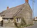 Old stone building with thatched roof on road junction.