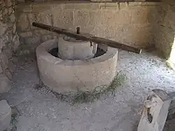A reconstructed olive press from Volubilis consisting of a circular stone basin with a circular stone inset, atop which a long wooden bar is fixed