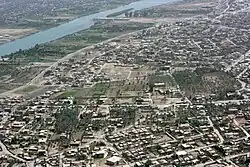 Aerial photograph of a built-up area, with a major river, houses, and palm groves.