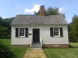 Small cottage with white walls, black door, and brick chimney