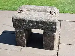 A large grey stone with two rings attached, propped up on two smaller stones.
