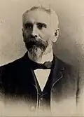 A black-and-white photograph of a man in a suit with a bow tie