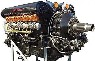 A front right view of a black-painted aircraft piston engine. The words 'Rolls-Royce' appear in red text on the camshaft cover.