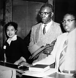A black and white photograph of Rosa Parks standing beside E. D. Nixon and Fred Gray.