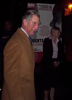 Charles in a brown coat attending the performance in Stratford-upon-Avon