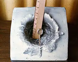 A 7-gram object (shown in center) shot at 7&nbsp;km/s (23,000&nbsp;ft/s), the orbital velocity of the ISS, made this 15&nbsp;cm (5.9&nbsp;in) crater in a solid block of aluminium.