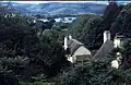 Thatched roofs of white painted houses nestled in tree filled valley.