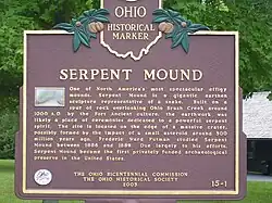 Ohio historical marker plaque for Serpent Mound, reads: "One of North America's most spectacular effigy mounds. Serpent Mound is a gigantic earthen sculpture representative of a snake. Built on a spur of rock overlooking Ohio Brush Creek around 1000 A.D. by the Fort Ancient culture, the earthwork was likely a place of ceremonies dedicated to a powerful serpent spirit. The site is located on the edge of a massive crater, possibly formed by the impact of a small asteroid around 300 million years ago. Frederic Ward Putnam studied Serpent Mound between 1886 and 1889. Due largely to his efforts, Serpent Mound became the first privately funded archaeological preserve in the United States.