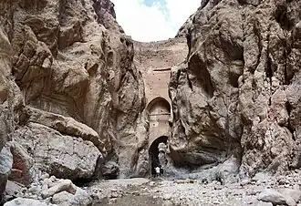 A tall, thin masonry dam positioned between two nearly vertical rock faces.