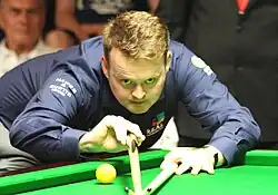 Shaun Murphy leaning over a table lining up a shot using a bridge stick
