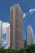 Ground-level view of a brown, rectangular high-rise; the window placement creates several horizontal bands on one side and one vertical stripe on the other