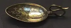 a short-handled spoon with fine detail marked in the bowl of the spoon of a cat-headed two-legged fish-tailed creature surrounded by fleur de lys
