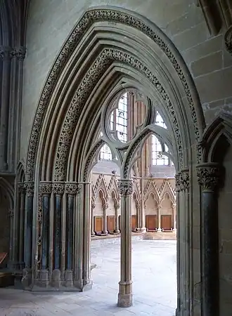 An elegant Gothic doorway opens into a chapter house. The arch of the doorway and the capital of its central pier have richly carved flowers.