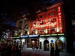 exterior of a London theatre at night, with large neon sign advertising The Mousetrap