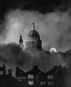 Black and White photograph of the dome of St Paul's, starkly lit, appearing through billowing clouds of smoke