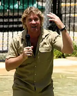 Irwin, who is wearing a khaki shirt and wristwatch, speaking into a handheld microphone