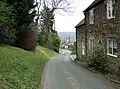 Street scene with a narrow road with houses on the right and trees on the left.