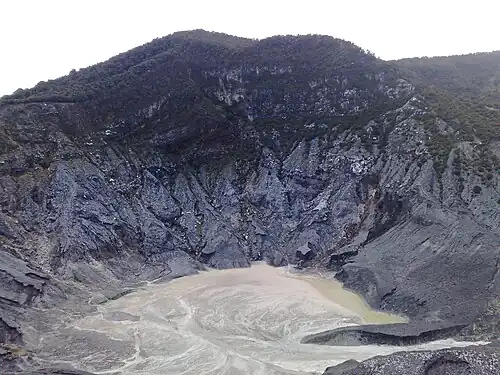 A photograph depicting a white sky at the top, a grey land configuration in the middle, and a body of water swirling around at the bottom.