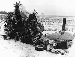 A tangled mass of metal with a wing and landing gear wheel barely recognizable, on a snowy field