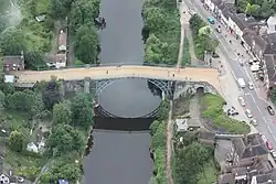 An aerial photo of the bridge, showing the close proximity of the main road alongside the river and the many building dotted nearby.