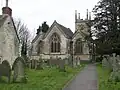 Gray three bay building with arched windows. Tower behind and gravestones in the foreground.