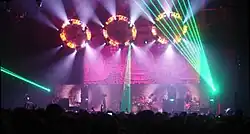 Musicians performing on stage in front of a crowd under many lights of different colors.
