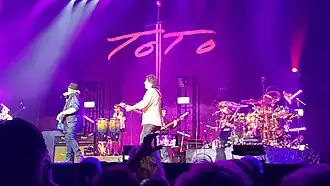 Toto performing in Middelkerke, Belgium in July 2022. From left to right: David Paich; Joseph Williams; Warren Ham; Steve Lukather; John Pierce; Robert "Sput" Searight