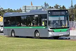 Light green, orange, and white bus stopping in front of multi-story building.